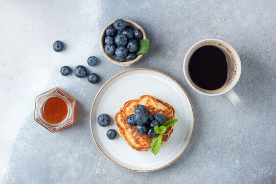 Top view pancakes with blueberries, honey and black coffee in cup. Breakfast meal