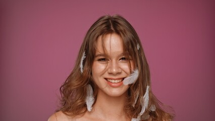 Smiling Girl with Feathers in Hair Against Pink Background