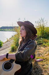 A girl with a guitar in cowboy style. Cowboy hat and boots. Sunny atmospheric photos.