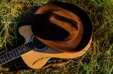 Classical guitar on the grass by the lake and a cowboy hat