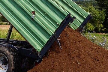 Close up of a tilted green metal trailer unloading a pile of soil onto the ground on a farm field...