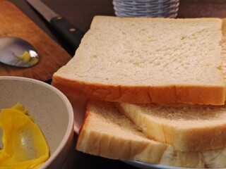 Sliced White Bread with Yellow Spread Knife and Spoon on Wooden Board.