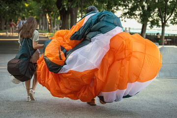 Paragliders carrying gear in park. Paragliders walk through park path with large wing folded in...