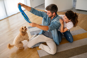 Happy couple playing with dog, having fun on floor at home. Married couple with cute pet