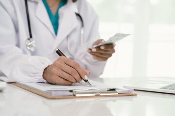 A doctor in a white coat uses a smartphone at a desk with a stethoscope, pills, medical documents, and a pen, focusing on healthcare communication and patient care.