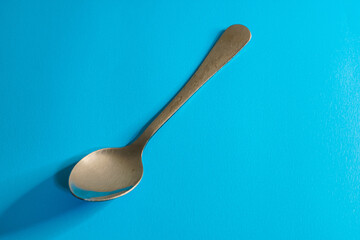 A single, silver spoon resting on a vibrant, solid blue surface, casting a shadow.