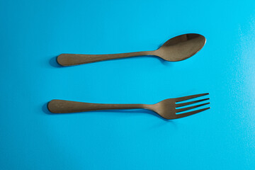 A close-up shot of a spoon and fork, placed on a vibrant blue surface.