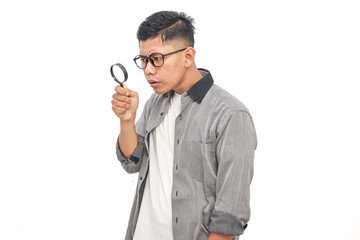 Curious Asian man intently examines something with a magnifying glass on white background