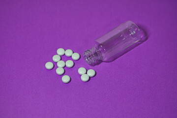 Scattered pills spill from a clear plastic bottle on a vibrant purple surface.