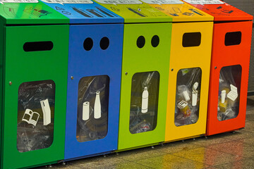 Colorful recycling bins for waste disposal, clearly labeled and partially filled with various...