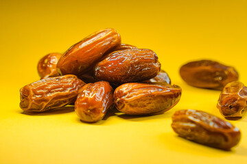 A pile of dried dates, some scattered around, are presented against a vibrant yellow background.