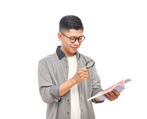 Man in glasses intently examining a book with a magnifying glass on white backdrop