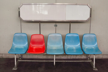 Five colorful chairs arranged in a row beneath a blank, rectangular sign.