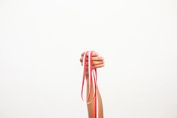 A hand holding red and white ribbons against a bright white background. Celebratory spirit