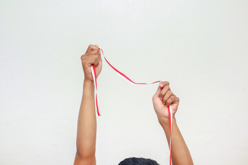 Hand holding red and white ribbon celebrating Indonesian Independence Day on white background, representing patriotism and national pride