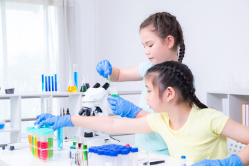 Asian girl and Caucasian girl concentrate on pipette handling and color preparation with teamwork,...