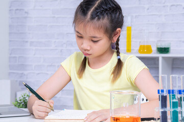 Science education concept with girl taking notes, experimenting with beaker liquids, elementary...