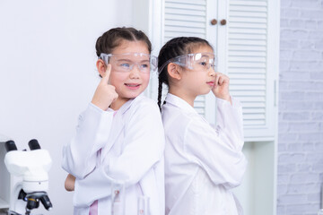 Portrait of two Asian children standing back-to-back in science class, dressed as scientists with goggles and lab coats, promoting collaboration, future goals, and shared curiosity in science learning