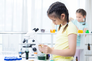 Asian child using dropper with black liquid during chemistry activity, lab table filled with...