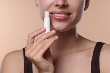 Young woman with lip balm on beige background, closeup
