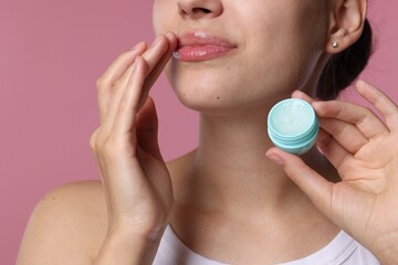 Young woman with lip balm on pink background, closeup