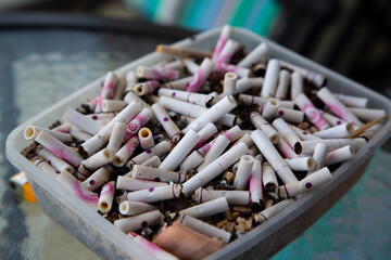 Close-up of a plastic container filled with cigarette butts and ash, symbolizing smoking addiction, pollution, and unhealthy lifestyle. Concept of waste and tobacco-related environmental damage