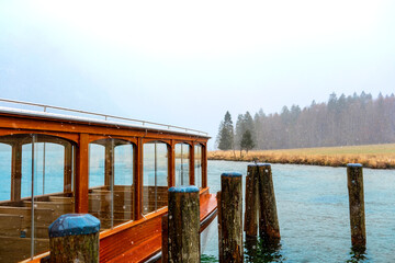 Wooden ferry docked during snowfall on mountain lake for winter, transport and seasonal lifestyle...