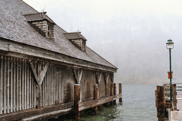 Rustic wooden boathouse by winter lake under snowfall for architecture, heritage and seasonal...