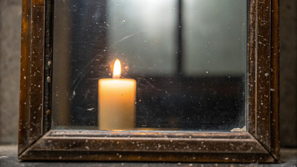 A lit candle reflected in a dirty old wooden mirror with romantic atmosphere