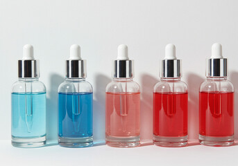 Naklejka premium Five dropper bottles filled with colorful liquids ranging from blue to red on a white background