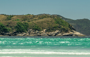 Fototapeta premium Beautiful beach das Conchas, close to the city of Cabo Frio, with blue sea around, sky with clouds and mountains in the background.