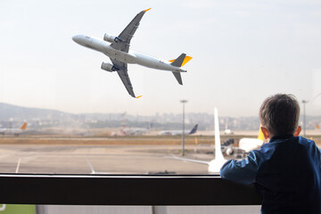 Kid watching planes taking off from airport window. Boy waiting for his flight. Aviation idea...