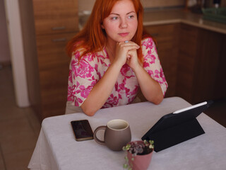 young woman working on tablet at home kitchen. with headache sitting at table. feeling stress...