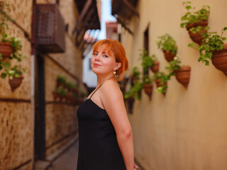 Young woman in elegant black dress walking in cozy old town Keleci, Antalya, Turkey during summer...