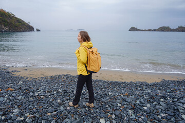 Woman walking near cloudy winter sea. Sitting on stones, watching sea waves, relaxing together,...