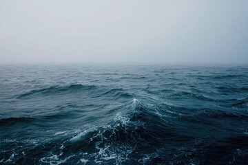 A misty, dark ocean scene with slightly choppy waves, a muted color palette dominated by deep blues and grays extending to a hazy horizon