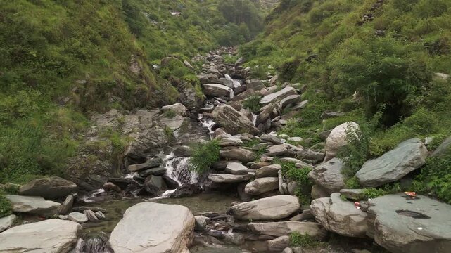 A slow motion wide angle aerial cinematic drone video of flying upstream over a smooth rocky waterfall with greenery by the sides in nature at Bhagsu falls, Mcleodganj, Himachal Pradesh, India, Asia