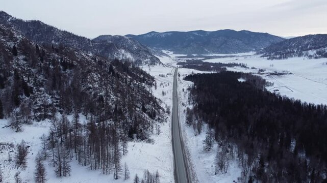 Aerial footage of a winding snow-covered road leading to Ust-Koksa in the Altai Republic, Russia. The video shows scenic winter landscapes with forests, hill