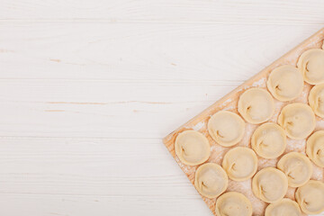 Raw dumplings with flour on wooden board and white table