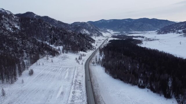 Aerial footage of a winding snow-covered road leading to Ust-Koksa in the Altai Republic, Russia. The video shows scenic winter landscapes with forests, hill
