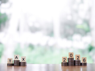 Wooden blocks with the word TAX, Number 2026 on stack of coins. The concept of prepare to pay tax...