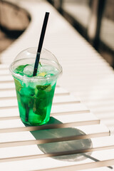 Refreshing green cocktail sitting on white bench in bright sunlight
