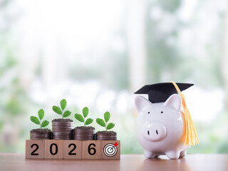 Piggy bank with graduation hat, Wooden block with number 2026 and plant growing on stack of coins....