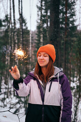 A young woman is celebrating Christmas in a snowy forest, holding a sparking sparkler.