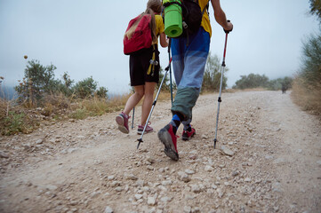 Energetic Young Hikers Exploring a Mountainous Trail with Trekking Poles, Backpacking Gear, and...