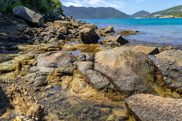 Part of Praia do Forno, with large moss-covered rocks, crystal clear waters and mountains in the...