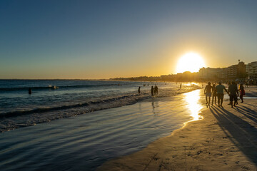Sunset, with the last rays of sunlight leaving a beautiful orange hue in the sky behind the city of Cabo Frio and in the sea waters full of swimmers. Rio de Janeiro, Brazil.