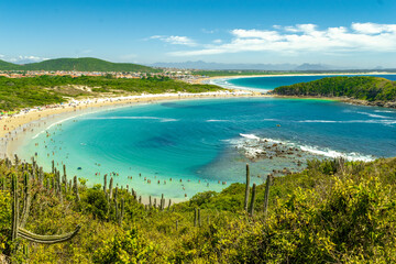 View from above of Concha Beach. With lots of vegetation and mountains around. Sea with crystal clear green waters and beautiful blue sky. Near the city of Cabo Frio, Rio de Janeiro.