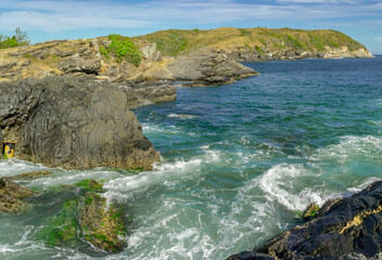 View of part of Praia do Forte, with many rocks and crystal clear waters all along the beach, mountains in the background and blue sky. Cabo Frio, Brazil