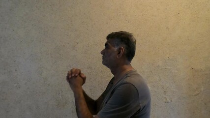 Side View of Graying Man With Light Beard Urgently Requesting by Pressing Hands Together Indoors Near Wall